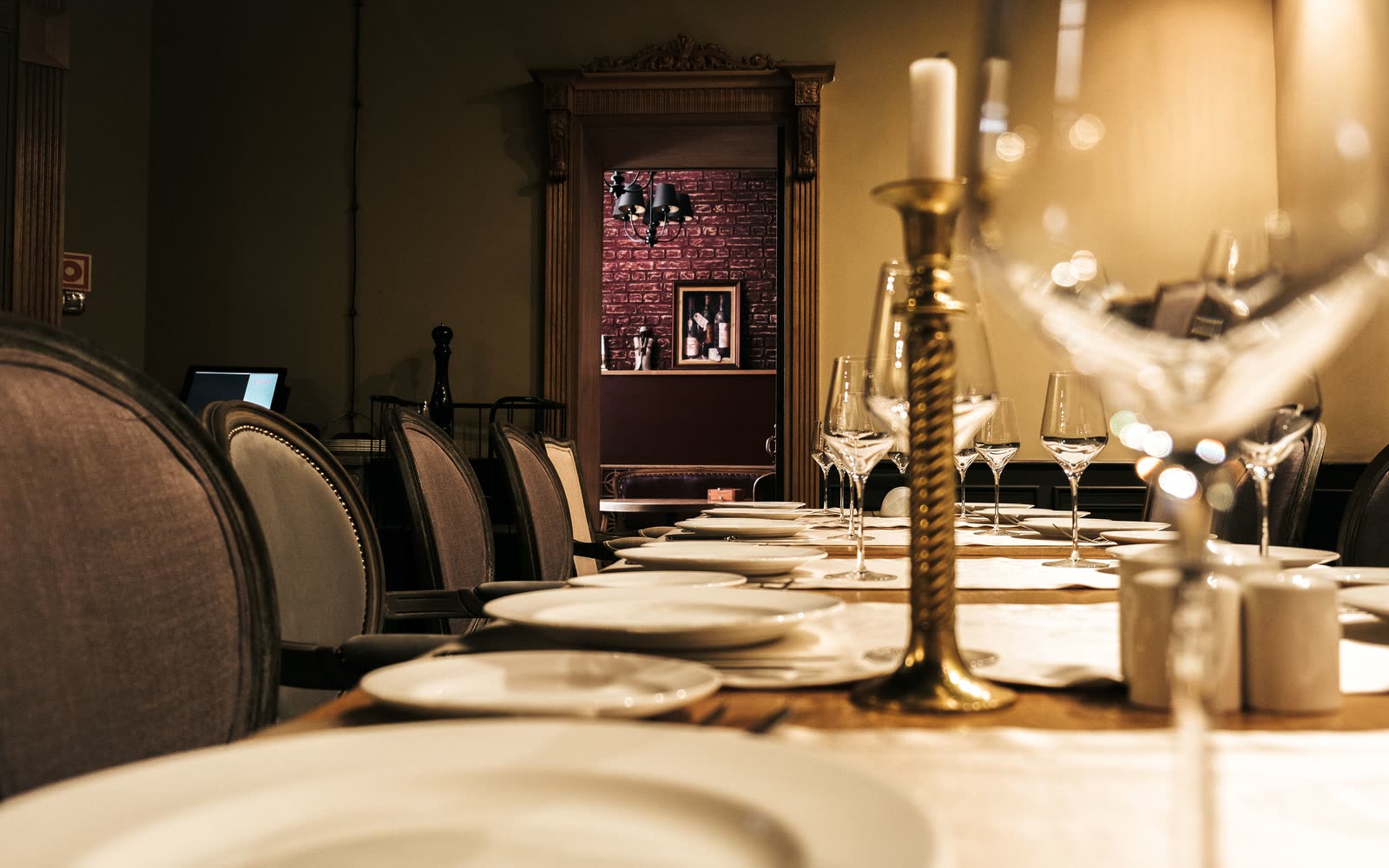 A long table laid for dinner, photographed down its length by candlelight, with the rest of the room dark behind it.
