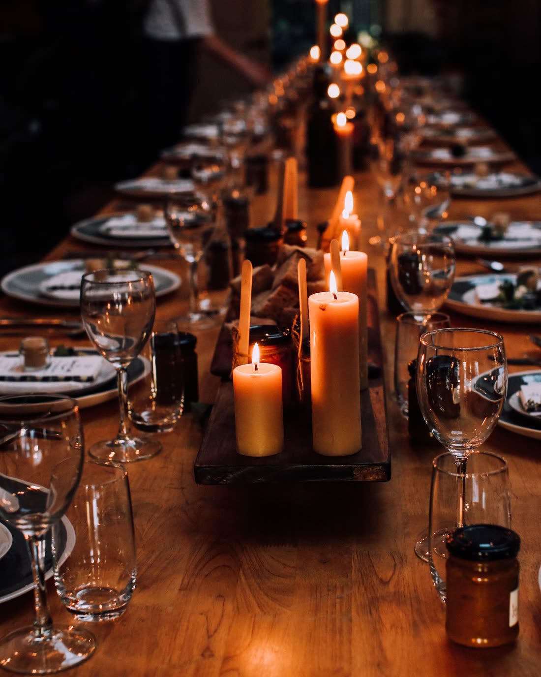 One long oak table seen from above, a row of pillar candles burning down the middle of it and places set either side.