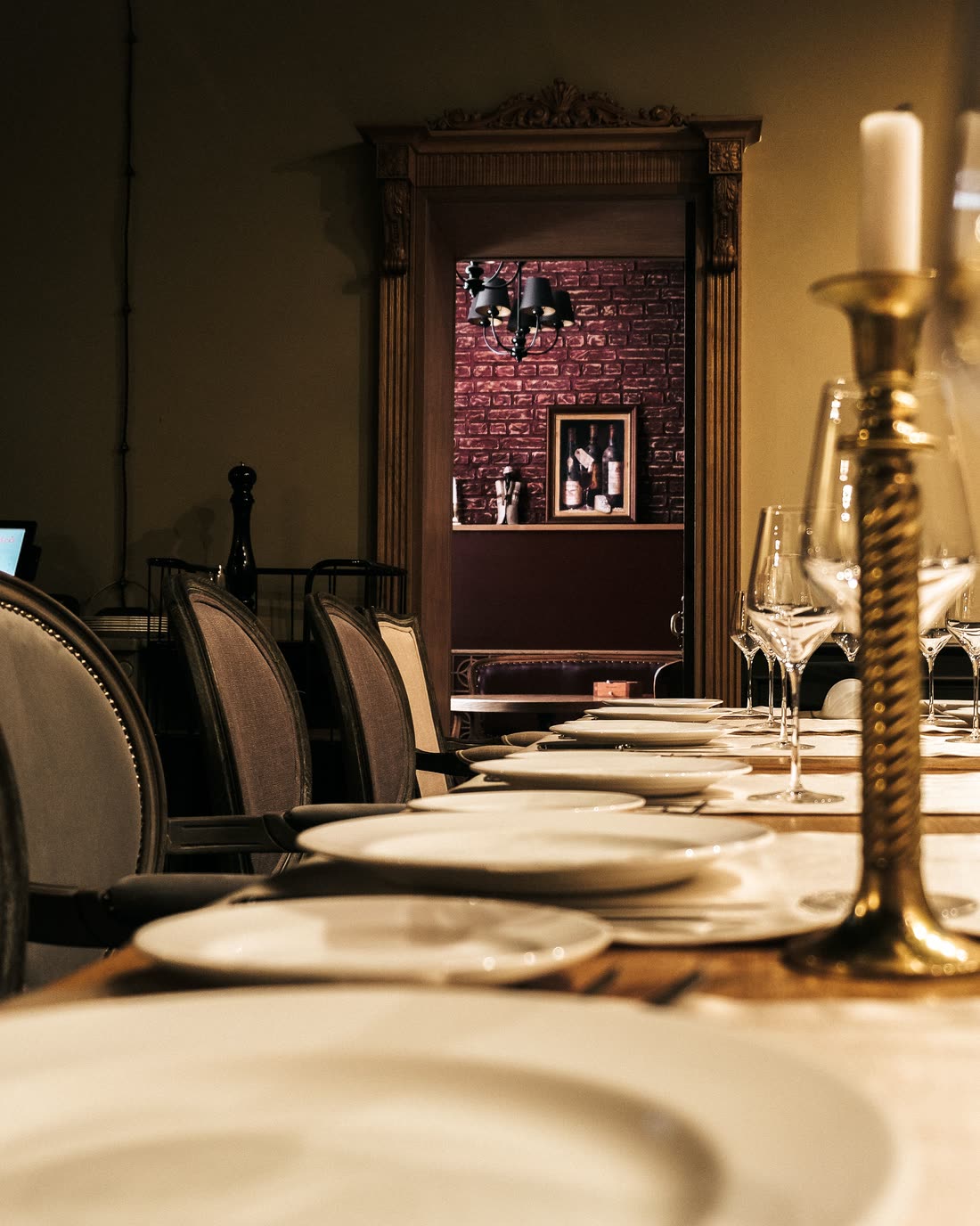 A long table laid for dinner, photographed down its length by candlelight, with the rest of the room dark behind it.